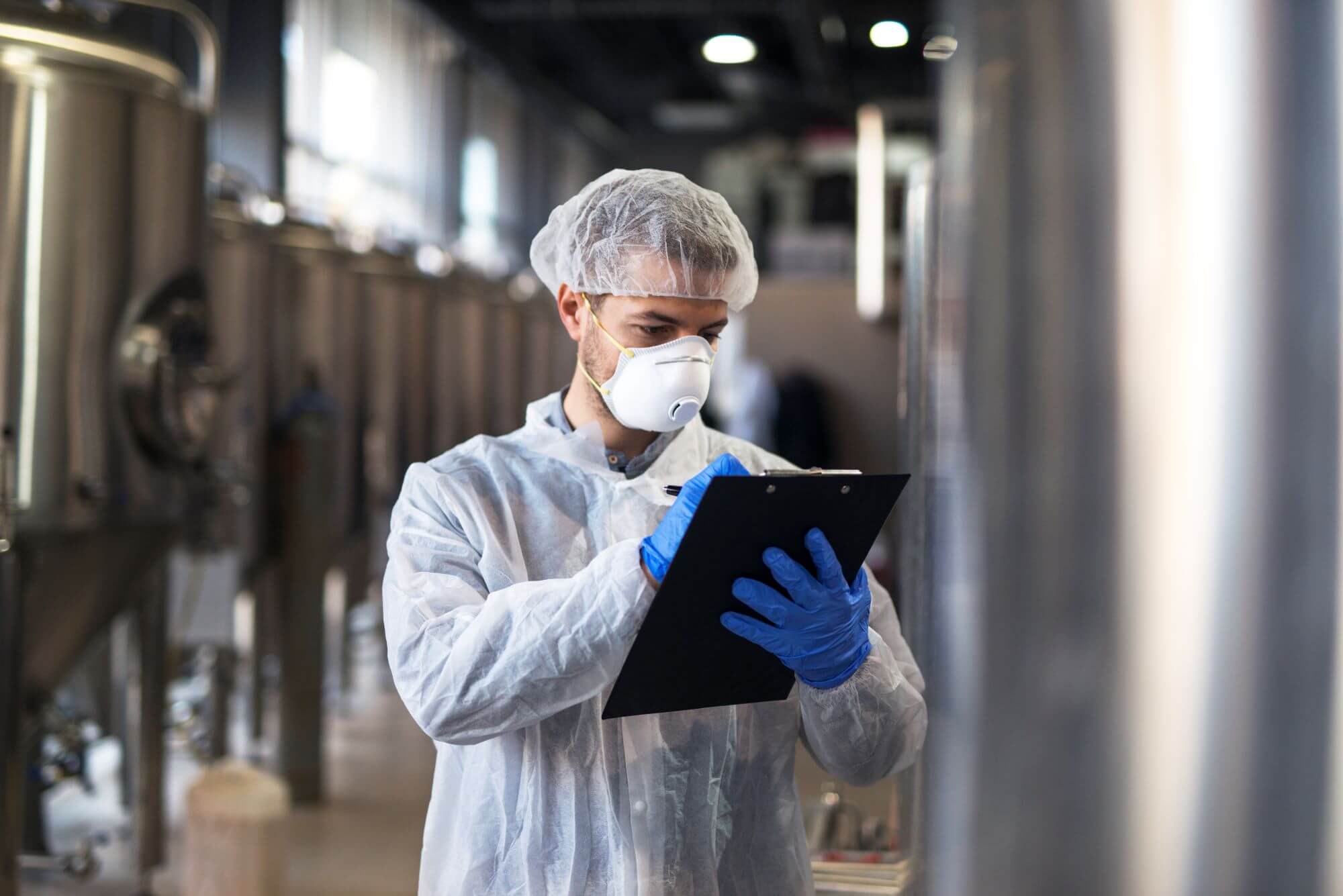 Clipboard-technologist-white-uniform-checking-quality-face-mask-production-factory-tank-inspection